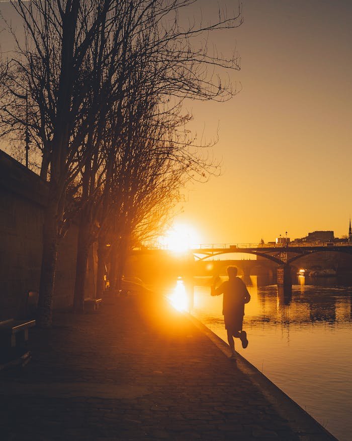 Silhouette of a man jogging along the Seine River in Paris during a vibrant sunset.